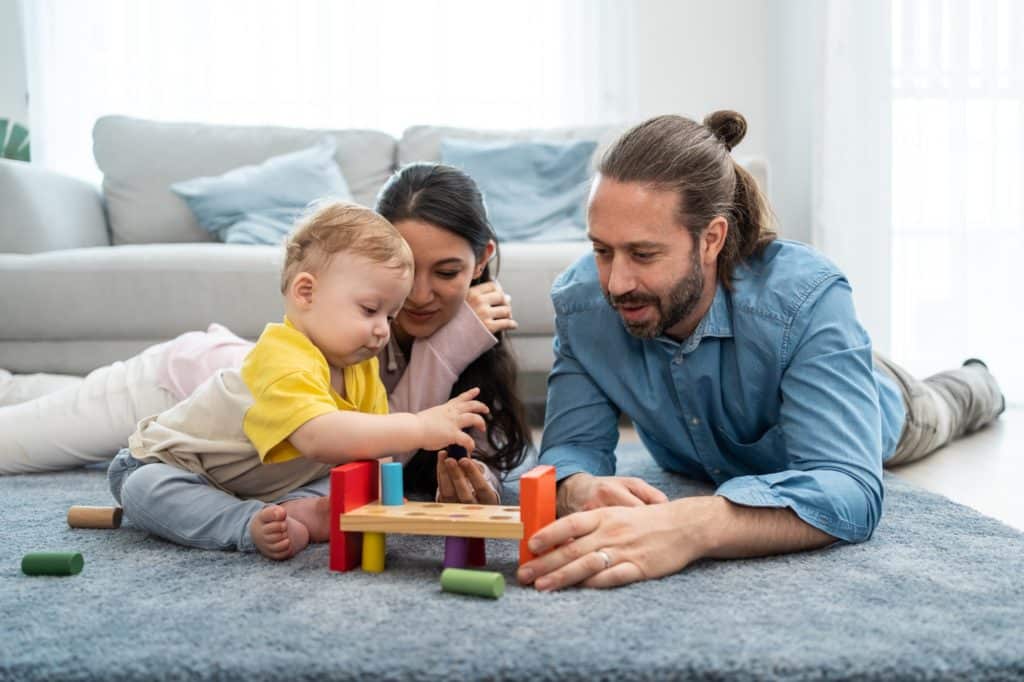 Caucasian mother and father looking to young baby child's development in house.