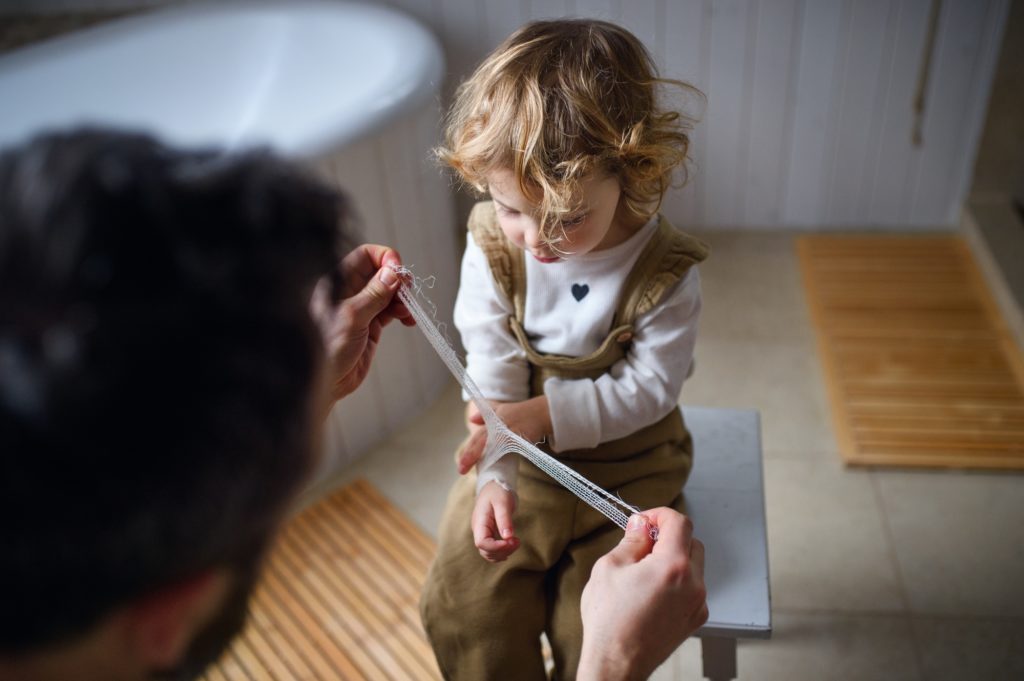 Father putting bandage on small hurt toddler child indoors at home