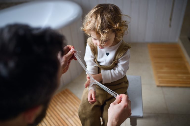 Father putting bandage on small hurt toddler child indoors at home